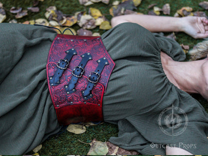 Person wearing a red leather corset with intricate designs, lying on the ground with leaves around. Elegant Floral Underbust Leather Corset - Handcrafted Rose Design for Larp, Reinassance Faire Cosplay