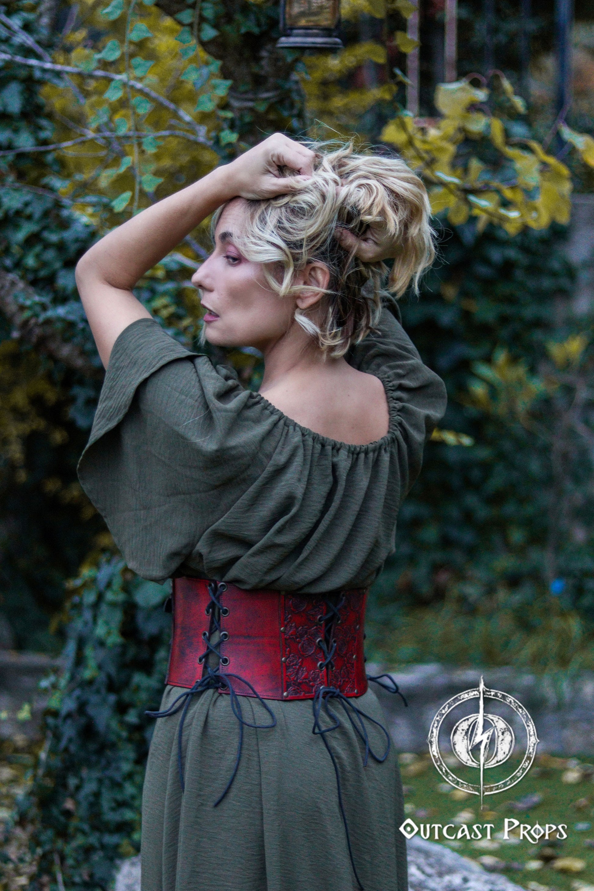 Woman in a green dress with a red corset standing outdoors with greenery in the background. Elegant Floral Underbust Leather Corset - Handcrafted Rose Design for Larp, Reinassance Faire Cosplay