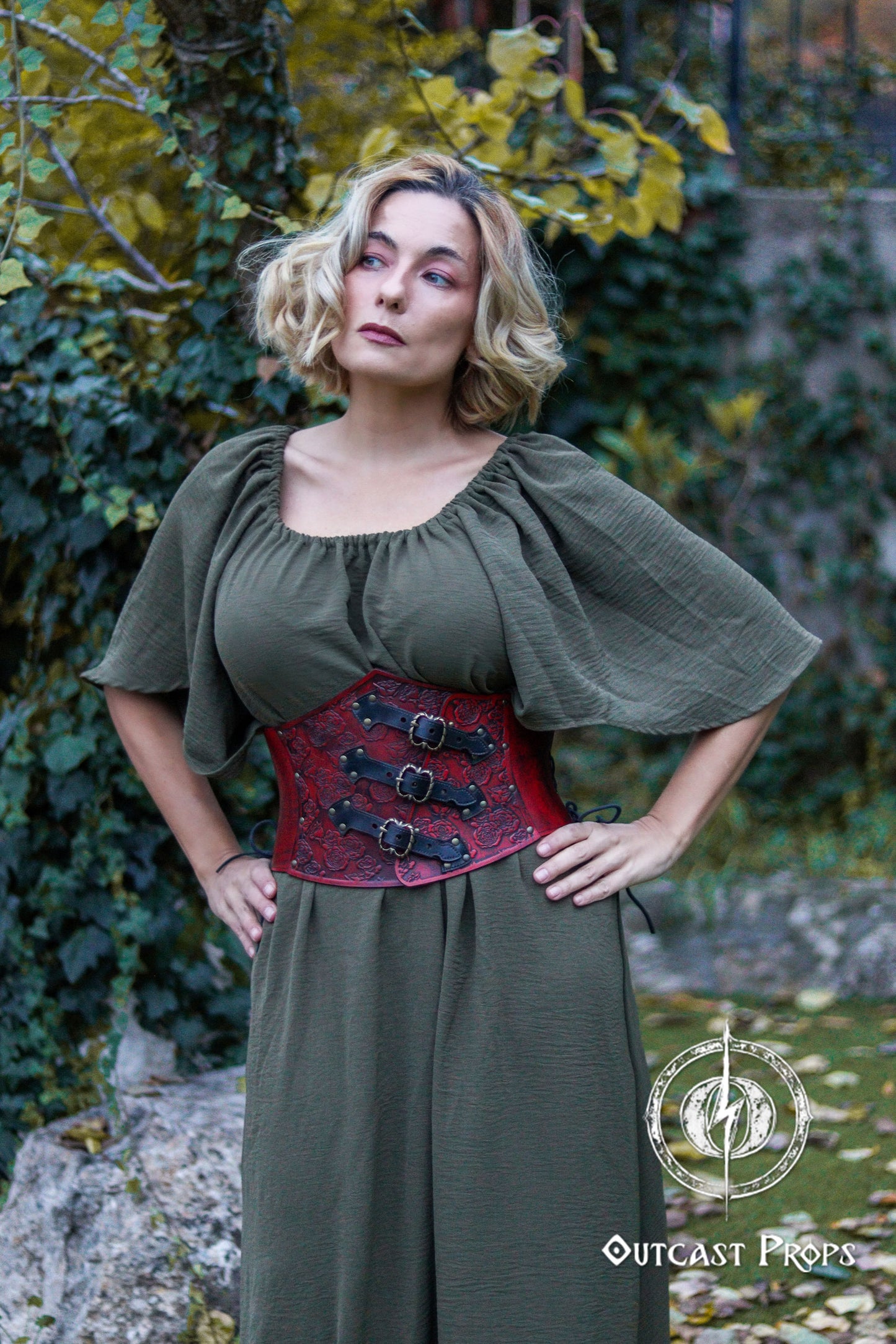 Woman wearing a green dress with a red leather corset against a natural background. Elegant Floral Underbust Leather Corset - Handcrafted Rose Design for Larp, Reinassance Faire Cosplay