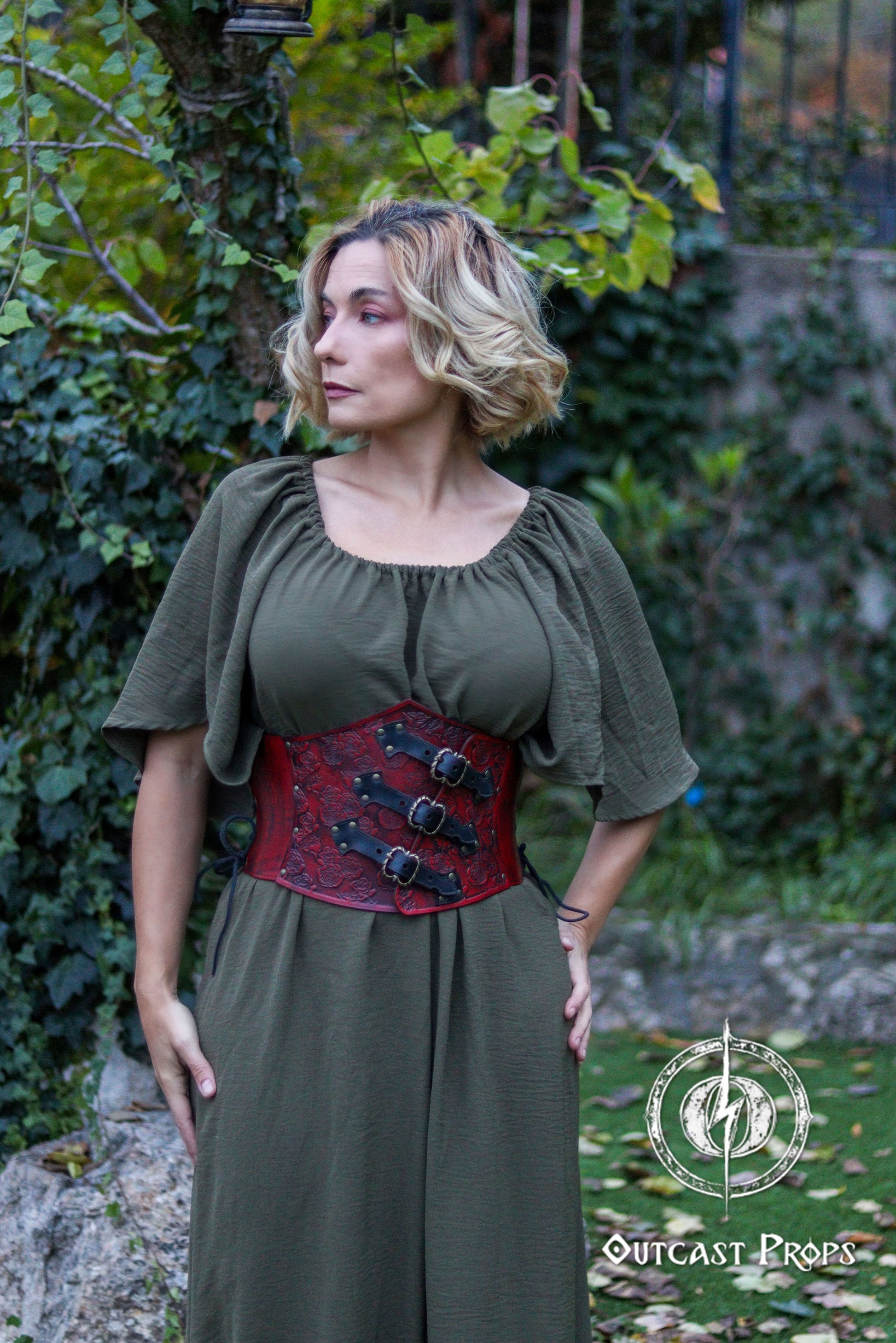 Woman wearing a green dress with a red corset belt standing outdoors. Elegant Floral Underbust Leather Corset - Handcrafted Rose Design for Larp, Reinassance Faire Cosplay