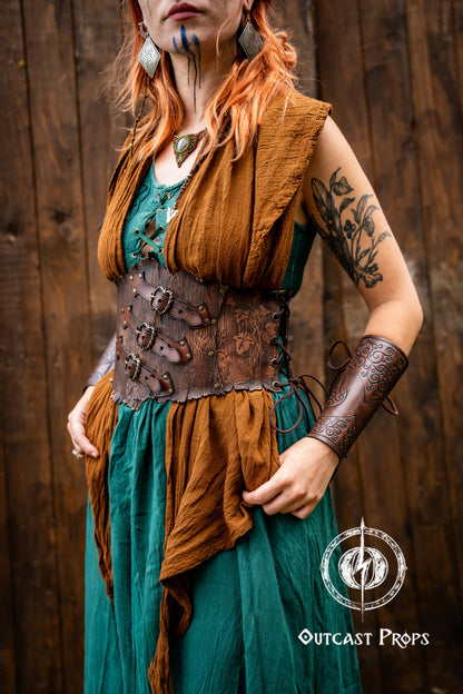 Person in a fantasy costume with 'Outcast Props' logo in the corner. Person wearing a detailed leather corset with decorative elements, branded 'Outcast Props'. Underbust Wood Leather Corset. Herbalist corset. Druid corset. Elven Corset. Ivy Corset.
