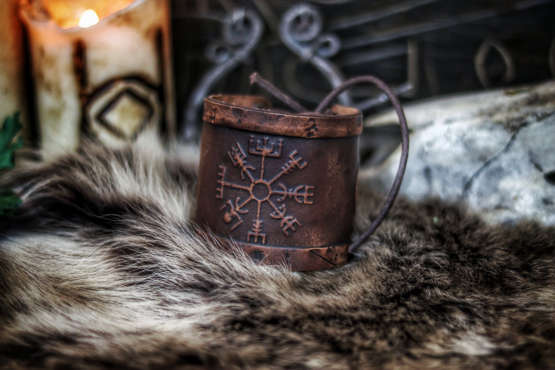 A brown leather wristband with a Viking compass design, displayed on a furry surface, featuring intricate handcrafted details. Vegvisir Leather Wristband, Galdrastafir Viking Bracelet,  Icelandic way finder rune leather embossed cuff, LARP, cosplay