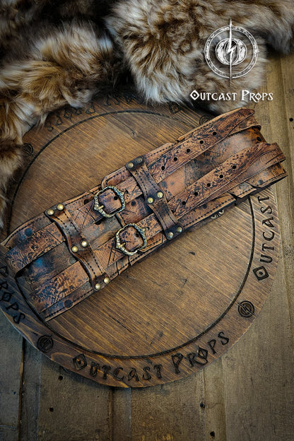 Brown leather belt with metal buckles on a wooden surface, branded 'Outcast Props'.   Veteran Leather Belt premium vegetable-tanned, worn by raiders and mercenaries.
