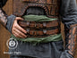 Person wearing a detailed leather armor vest with visible Outcast Props. Close-up of a detailed costume with leather straps and a green cloth, branded 'Outcast Props'.  Veteran Leather Belt premium vegetable-tanned, worn by raiders and mercenaries.branding.