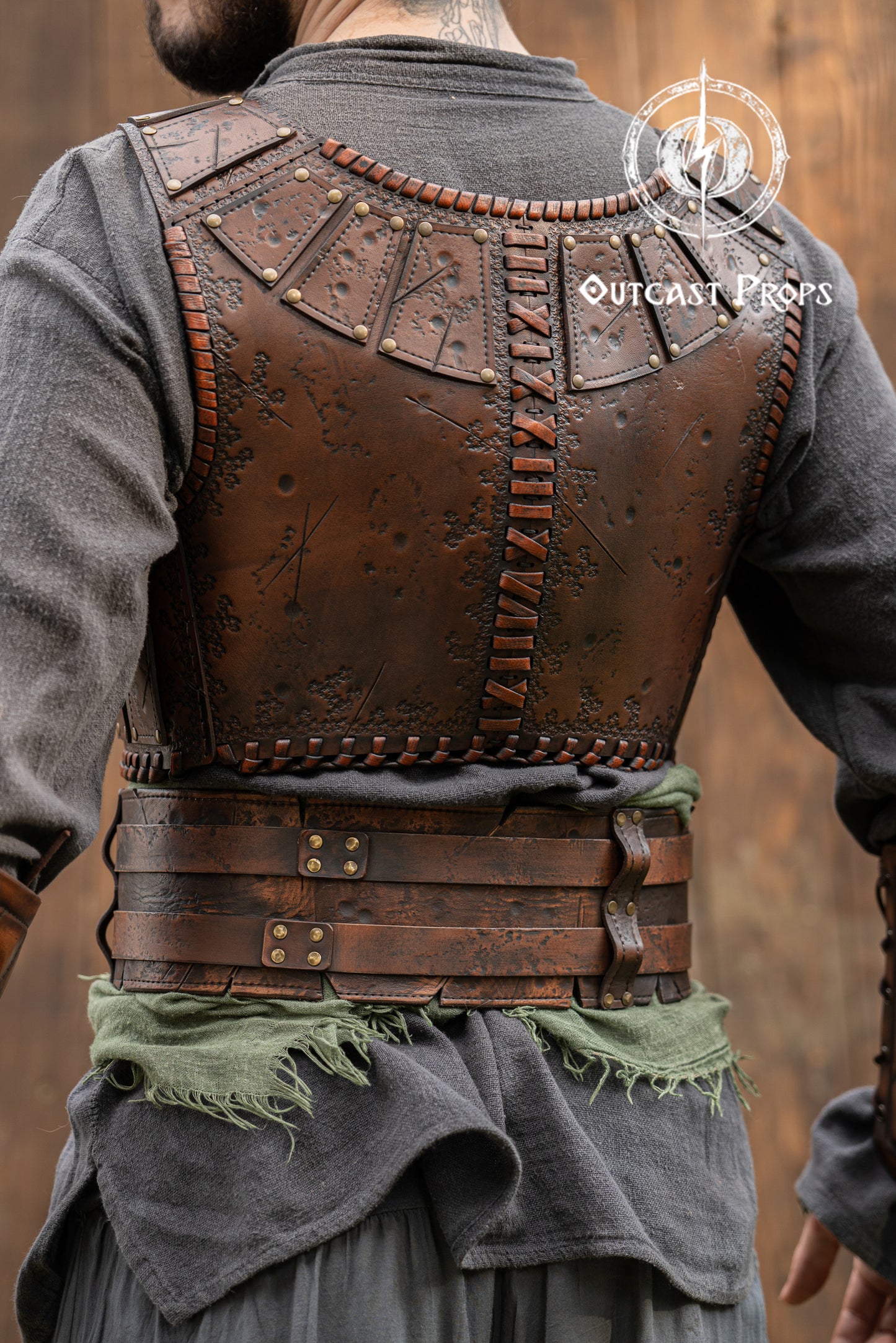 Person wearing a detailed leather vest with 'Outcast Peaks' branding. Close-up of a detailed costume with leather straps and a green cloth, branded 'Outcast Props'.  Veteran Leather Belt premium vegetable-tanned, worn by raiders and mercenaries.