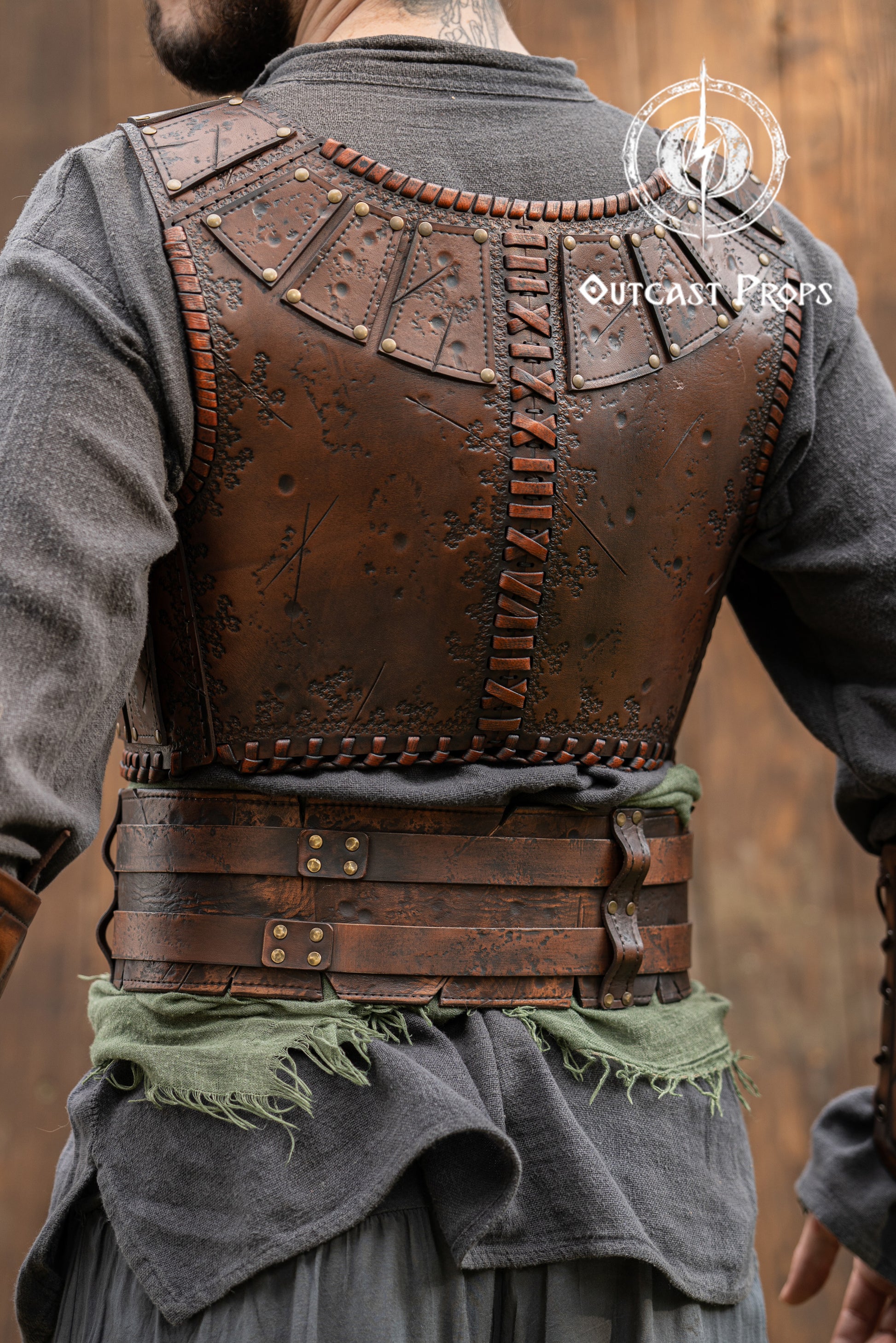 Person wearing a detailed leather vest with 'Outcast Peaks' branding. Close-up of a detailed costume with leather straps and a green cloth, branded 'Outcast Props'.  Veteran Leather Belt premium vegetable-tanned, worn by raiders and mercenaries.