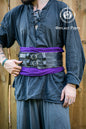 Person wearing a dark outfit with a purple sash and black leatrher broadbelt with Outcast Props logo in the corner. Veteran Leather Belt premium vegetable-tanned, worn by raiders and mercenaries.