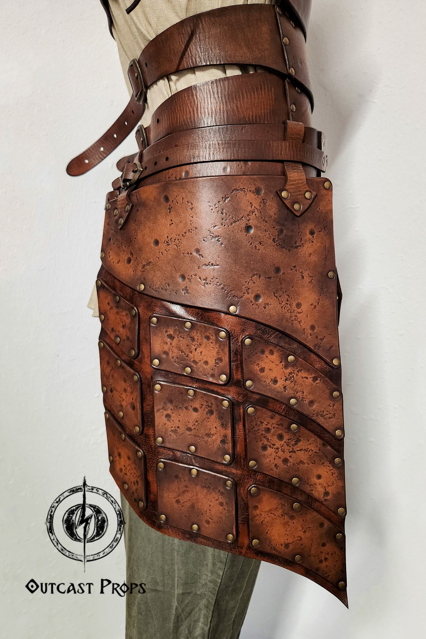 Close-up side view of brown leather tassets with brass rivets and distressed finish. Perfect for female warrior costumes, this handcrafted element of a LARP armor set provides protection and mobility for fantasy, viking or ranger characters.