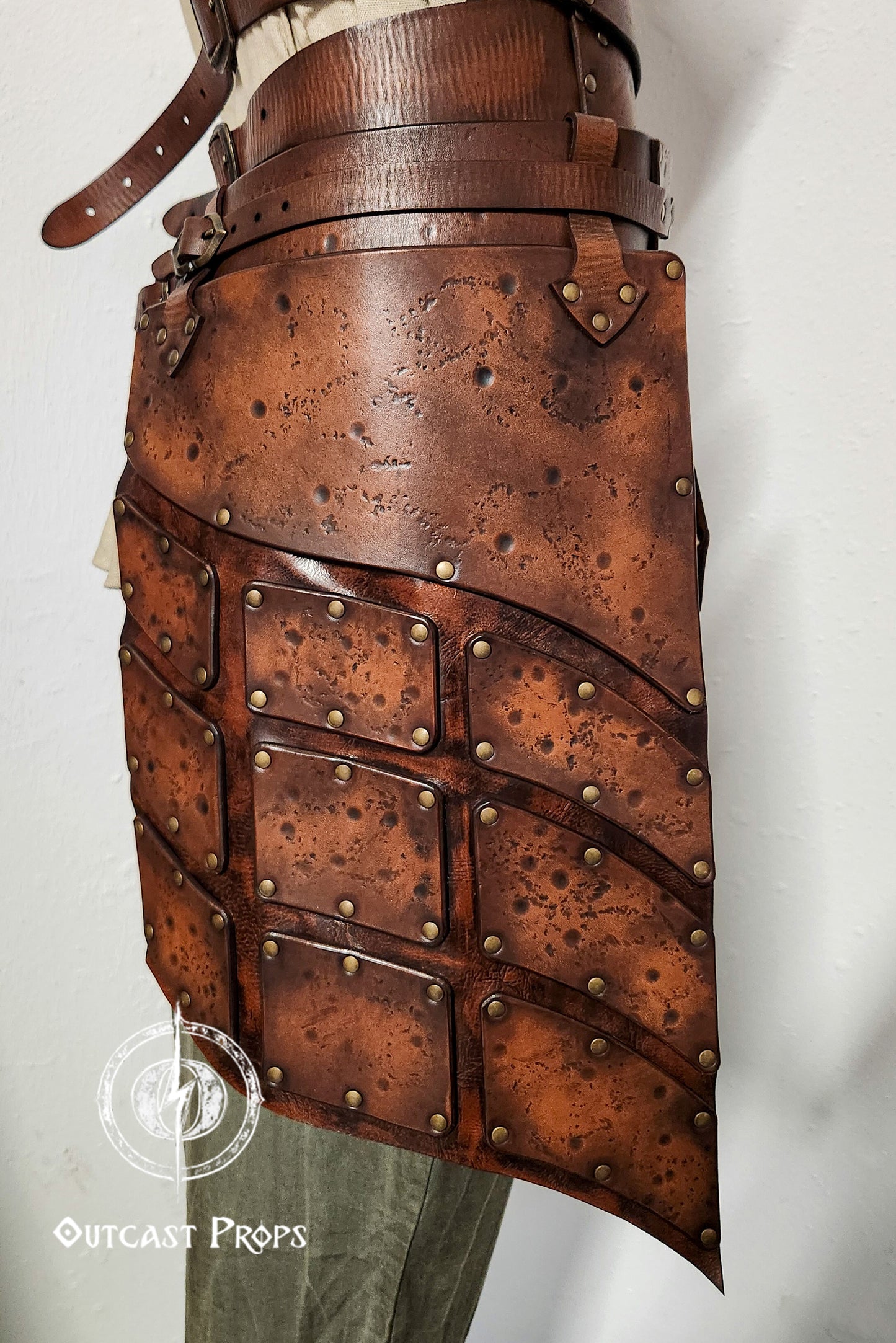 Close-up side view of brown leather tassets with brass rivets and distressed finish. Perfect for female warrior costumes, this handcrafted element of a LARP armor set provides protection and mobility for fantasy, viking or ranger characters.