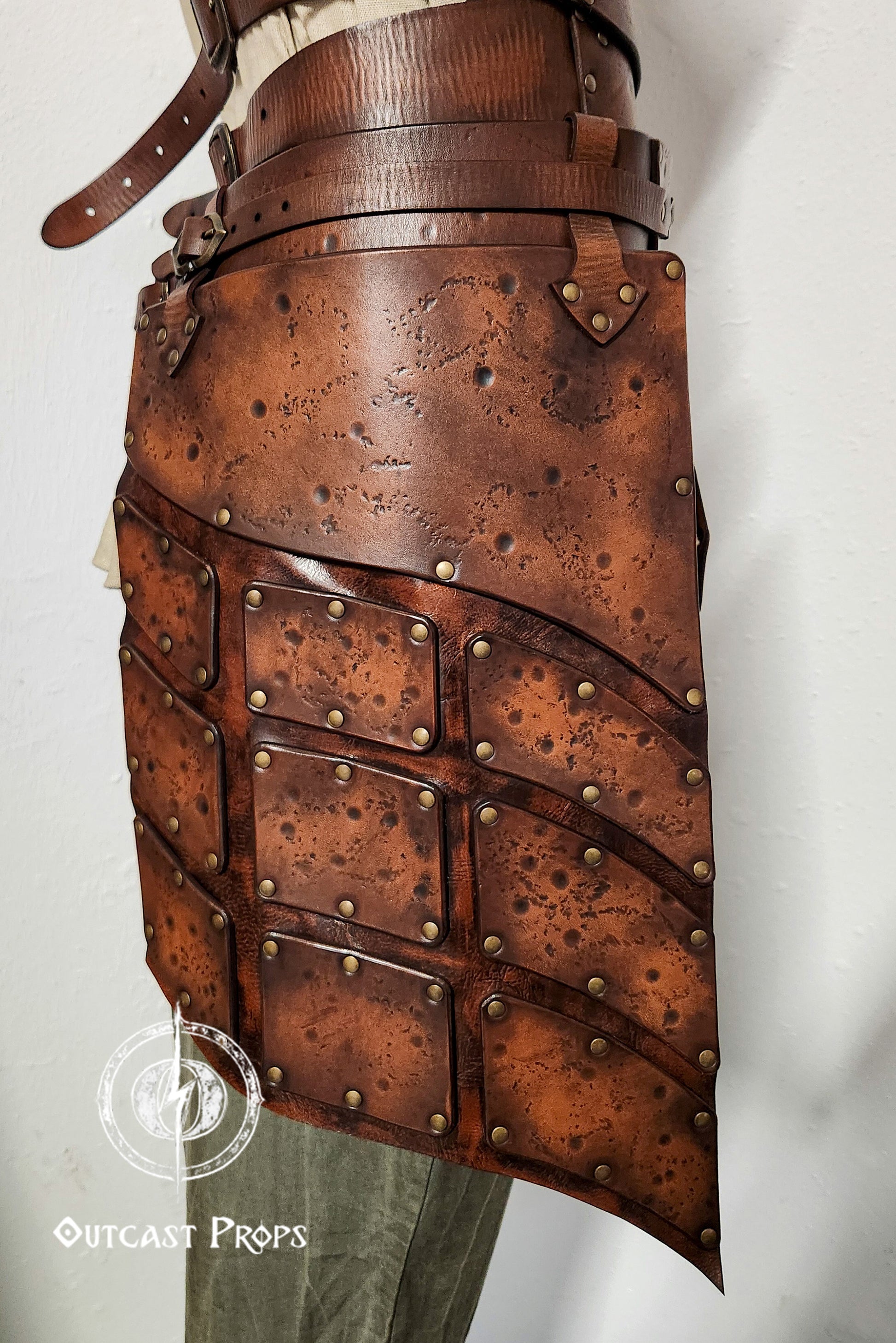Close-up side view of brown leather tassets with brass rivets and distressed finish. Perfect for female warrior costumes, this handcrafted element of a LARP armor set provides protection and mobility for fantasy, viking or ranger characters.