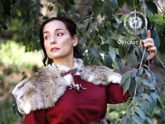 LARP model in woodland surroundings wearing a soft brown and white Viking fur mantle with leather closure. Paired with red medieval clothing and horned skull necklace, this handmade shoulder cape is perfect for fantasy priestess cosplay, barbarian characters, or Celtic-inspired costumes. Great for Renaissance fairs, Viking reenactments or tribal LARP roles. Warm and immersive design.