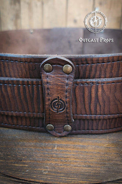 Close-up of a leather belt with metal fastenings on a wooden surface, branded 'Outcast Props'. Brown leather belt with brass buckle on a wooden surface, branded 'Outcast Props'. Medieval broadbelt for larp or cosplay. Elegant leather belt. 