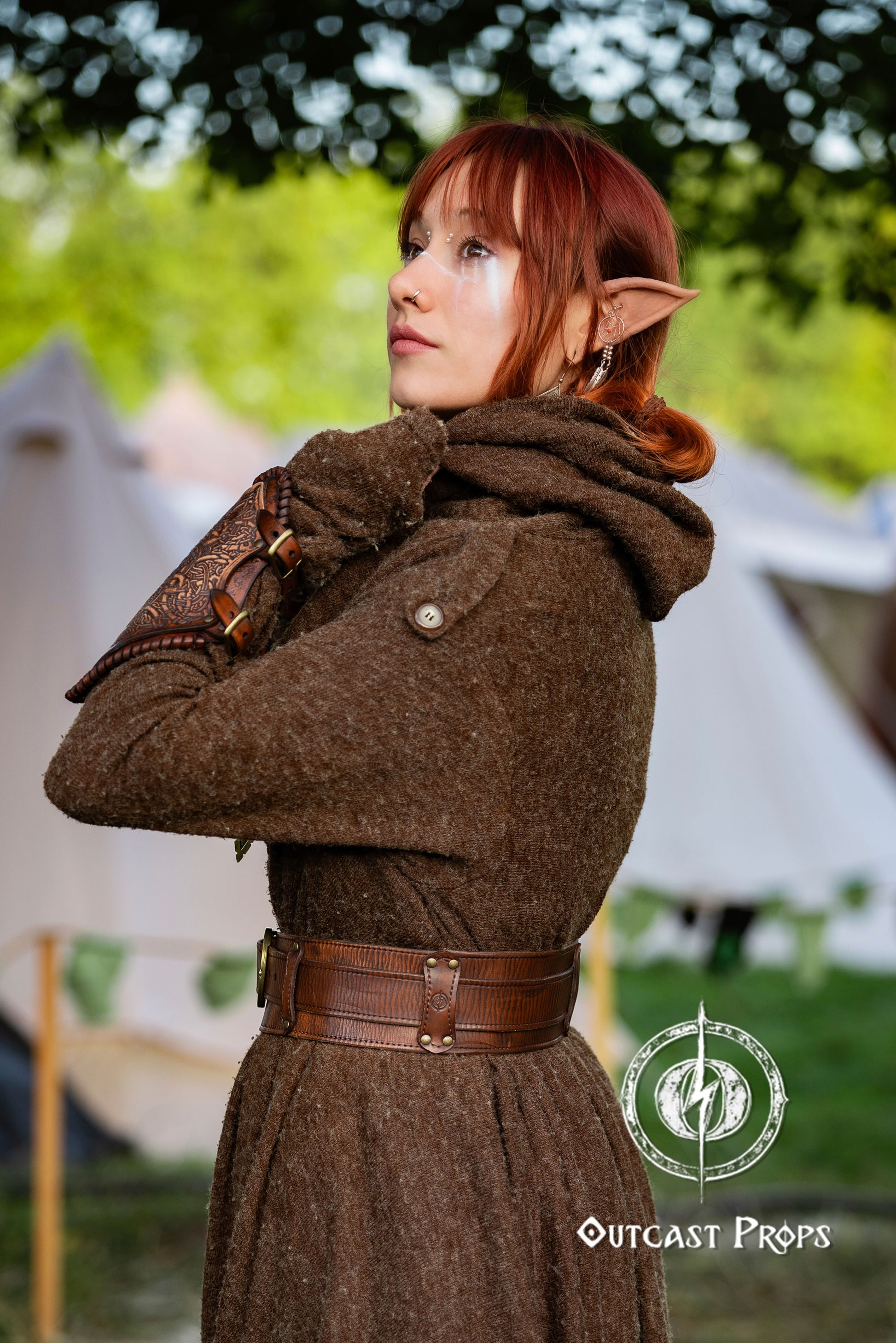 Person wearing a brown coat with a belt, standing outdoors with blurred tents in the background. Celtic knot leather belt silver buckle larp belt for ren fair fantasy costume celtic belt unisex leather belt for renaissance outfit