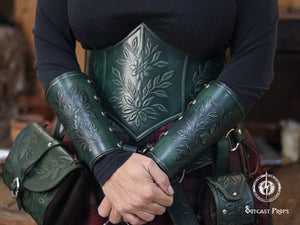 The Wildflower leather bracers in aged green are worn together with a matching embossed corset and bags, creating a full fantasy outfit. The floral pattern appears across all pieces, forming a coordinated renaissance faire look. Ideal for larp cosplay accessory sets, elven herbalist witch costumes and nature themed characters. The scene highlights the handcrafted botanical leatherwork and how the bracers fit comfortably on the forearms.
