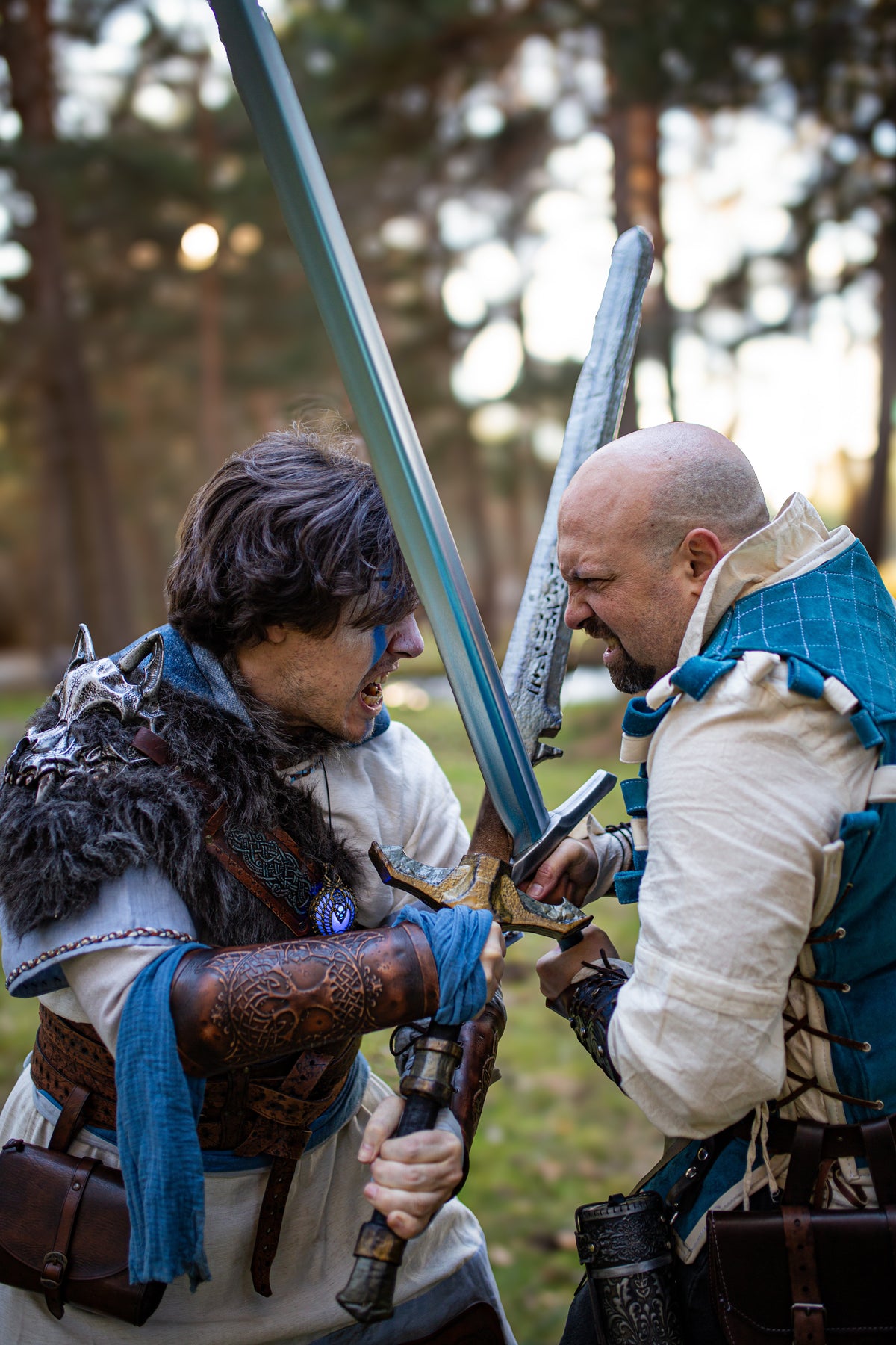 Dramatic forest battle scene between two fantasy warriors. The one with blue war paint wears brown leather bracers with Yggdrasil tree embossing, ideal for nordic warrior costume, viking leather bracers for larp, battle-ready cosplay armor, or medieval roleplay accessories. The dynamic action and intense expressions create a vivid moment of combat storytelling.