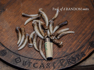 A close group of many resin fang tusks displayed on a wooden surface with a lighter included for size reference. The tusks vary in shape and tone, all hand painted to resemble aged bone, ideal for cosplay prop supplies, diy fantasy crafting, tribal decorations, nature inspired costumes, shaman accessories, creature design components and handmade props. Random mix of pieces for creative projects.