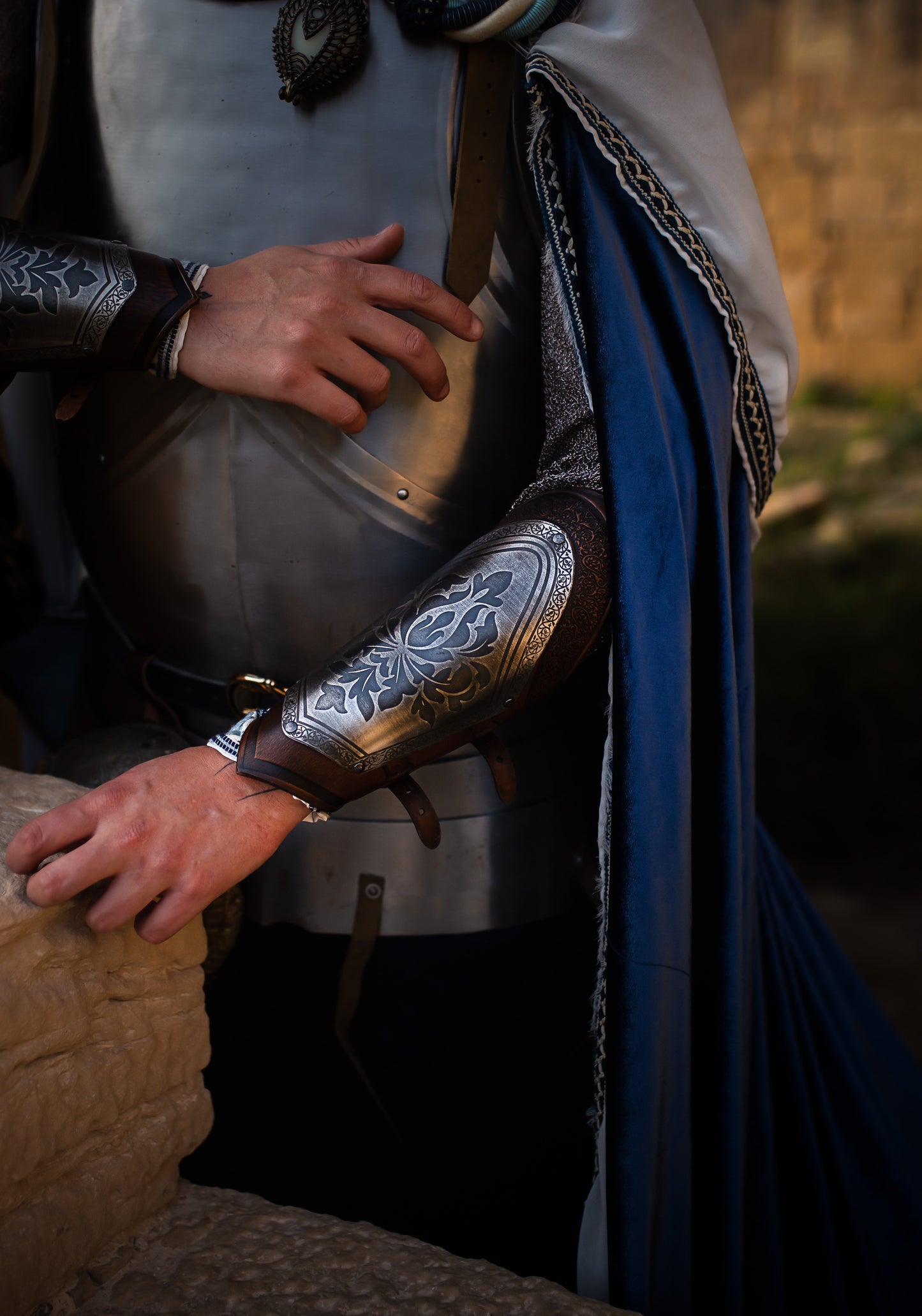 Close-up of a medieval knight costume showing detailed engraved leather bracers with silver metal plates, floral motifs, and leather straps. Perfect for fantasy cosplay, LARP armor, or noble character outfits. The texture of the armor and natural light enhance the historical look. Ideal accessory for renaissance fair or fantasy roleplay events.