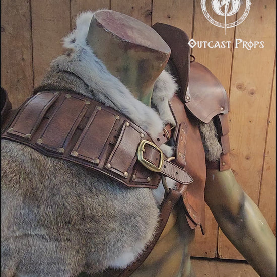 Leather barbarian armor set displayed on a muscular torso mannequin, featuring shoulder pauldrons, a chest harness, and thick grey rabbit fur mantle. Made from vegetable-tanned leather in aged brown tone, with weathered straps and metal buckles. Ideal for LARP, Viking cosplay or post-apocalyptic costumes. The fur and armor layers create a battle-worn barbarian look, full of texture and realism.
