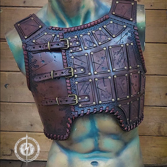 A handmade leather studded armor displayed on a stand, featuring chest plates with studs and an adjustable buckle system,. The armor has a brown distressed finish and is positioned against a backdrop with autumn leaves. A handmade leather studded armor displayed on a wooden stand with a fur cape, featuring brown leather plates with studs, and a corded edge finish. Barbarian studded leather chest armor with rabbit fur cape attachment shown on mannequin. Perfect for fantasy LARP, Viking