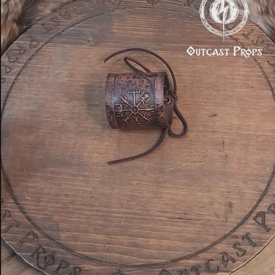 A brown leather wristband with a Viking compass design, displayed on a furry surface, featuring intricate handcrafted details. Vegvisir Leather Wristband, Galdrastafir Viking Bracelet,  Icelandic way finder rune leather embossed cuff, LARP, cosplay
