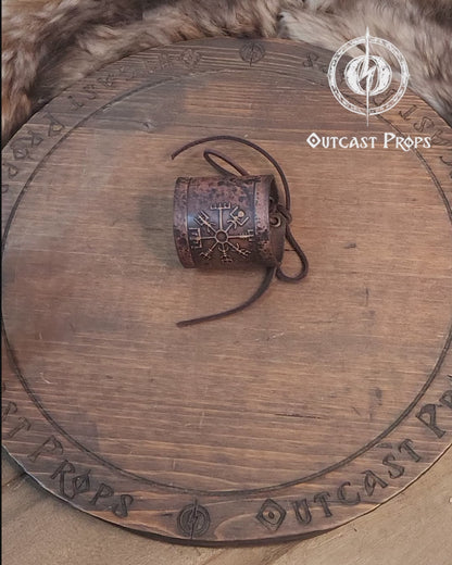 A brown leather wristband with a Viking compass design, displayed on a furry surface, featuring intricate handcrafted details. Vegvisir Leather Wristband, Galdrastafir Viking Bracelet,  Icelandic way finder rune leather embossed cuff, LARP, cosplay