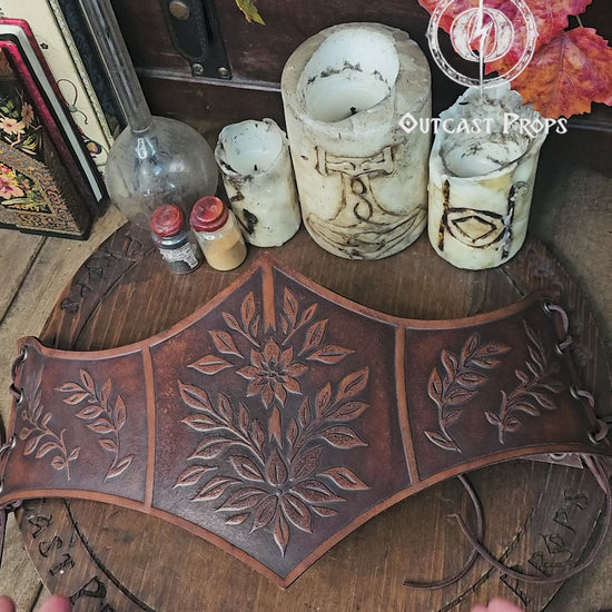 Floral embossed leather underbust corset in aged brown, crafted from premium vegetable tanned leather and worn as part of a Renaissance Faire outfit. The image highlights the detailed leaf carvings, ideal for elves, witches, herbalists or nobles at LARP or renfaire events. Below the corset, a matching belt and coin pouches complete the elegant medieval fantasy look while keeping essentials close during immersive roleplay.