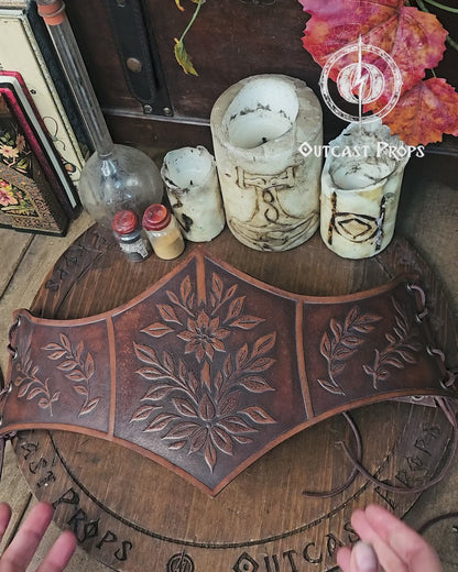 Floral embossed leather underbust corset in aged brown, crafted from premium vegetable tanned leather and worn as part of a Renaissance Faire outfit. The image highlights the detailed leaf carvings, ideal for elves, witches, herbalists or nobles at LARP or renfaire events. Below the corset, a matching belt and coin pouches complete the elegant medieval fantasy look while keeping essentials close during immersive roleplay.