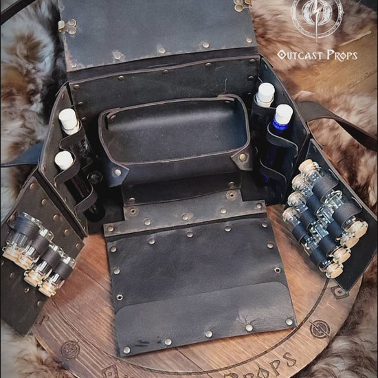 Fantasy Alchemist Bag made of natural leather, shown fully open with potion bottles, vials, and scrolls in a medieval apothecary setting. Perfect for LARP, steampunk, or cosplay characters like healers, mages, witches, or rogues. The bag includes secured compartments for bottles and a tray for tools, with quick access to emergency potions. Handmade and dyed by Outcast Props, combining practicality and immersive style for any roleplay adventure.