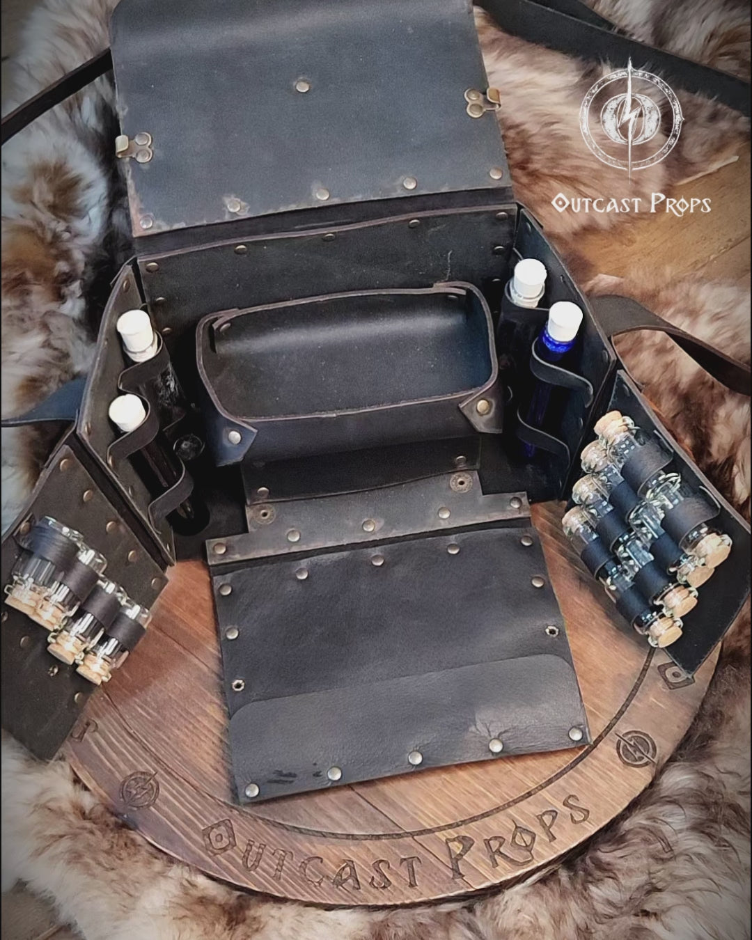 Fantasy Alchemist Bag made of natural leather, shown fully open with potion bottles, vials, and scrolls in a medieval apothecary setting. Perfect for LARP, steampunk, or cosplay characters like healers, mages, witches, or rogues. The bag includes secured compartments for bottles and a tray for tools, with quick access to emergency potions. Handmade and dyed by Outcast Props, combining practicality and immersive style for any roleplay adventure.
