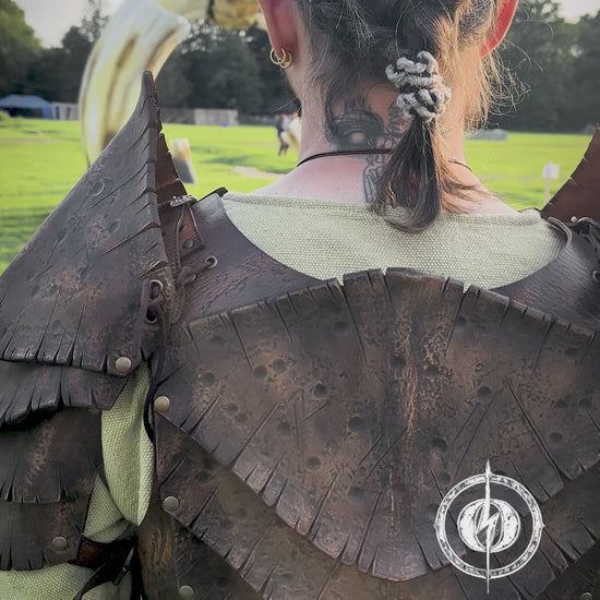 Back view of a warrior wearing the Dragon Scales Armor Set, standing before a giant bone-like sculpture at a LARP event. The armor is handmade from premium vegetable-tanned leather, textured to mimic ancient dragon hide. Shoulder guards and layered plates give a fierce, battle-ready look, ideal for cosplay, fantasy photoshoots, and immersive roleplay at Ren Faires or Viking festivals.