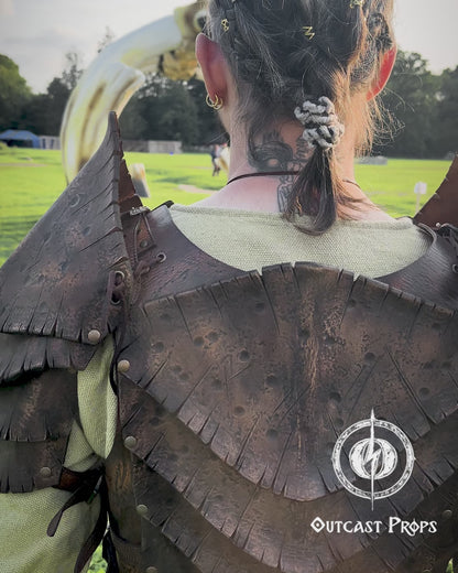 Back view of a warrior wearing the Dragon Scales Armor Set, standing before a giant bone-like sculpture at a LARP event. The armor is handmade from premium vegetable-tanned leather, textured to mimic ancient dragon hide. Shoulder guards and layered plates give a fierce, battle-ready look, ideal for cosplay, fantasy photoshoots, and immersive roleplay at Ren Faires or Viking festivals.