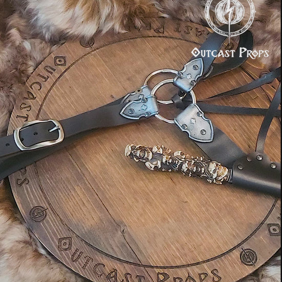 A black and silver leather wand holster with dual metal rings and riveted construction. Styled for Voldemort-inspired cosplay or LARP magic duels. Crafted for comfort and realism in wizard costumes, especially for Harry Potter fans recreating Death Eater aesthetics.Magic-style leather belt with decorative elements on a wooden surface, featuring Outcast Props branding.