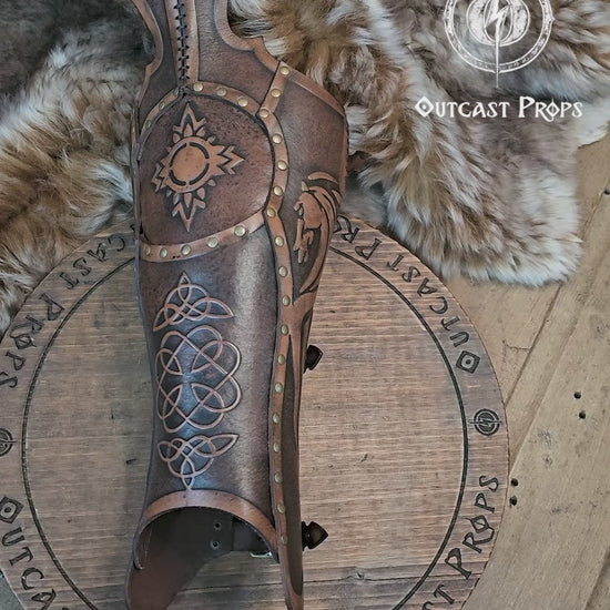 Single handcrafted Celtic leather greave resting on fur, embossed with knotwork and solar symbols recalling the heritage of Rohirrim riders and Viking leg armor. Made from vegetable-tanned leather aged by hand, with brass rivets and sculpted edges. Perfect for fantasy LARP, horsemen, and medieval reenactment costumes seeking authentic, eco-friendly craftsmanship and the distinctive aged finish of Outcast Props.