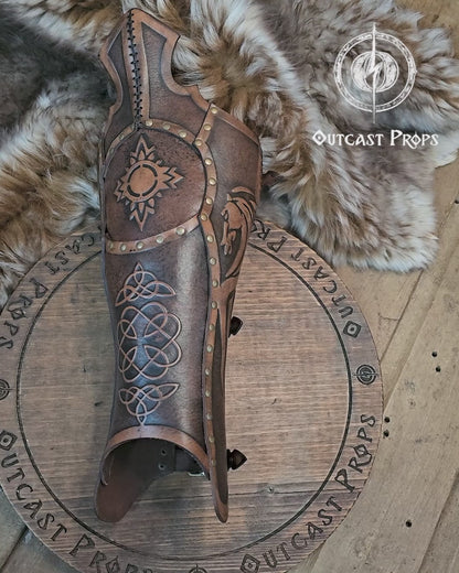 Single handcrafted Celtic leather greave resting on fur, embossed with knotwork and solar symbols recalling the heritage of Rohirrim riders and Viking leg armor. Made from vegetable-tanned leather aged by hand, with brass rivets and sculpted edges. Perfect for fantasy LARP, horsemen, and medieval reenactment costumes seeking authentic, eco-friendly craftsmanship and the distinctive aged finish of Outcast Props.