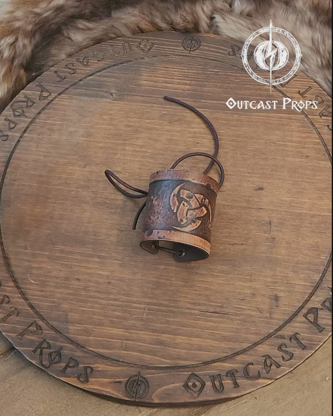 Leather cuff bracelet with the Three Horns of Odin design, placed against a backdrop with candles and decorative foliage. Horns of Odin Leather Cuff Bracelet, Viking Bracer, leather embossed wristband, stamped viking pattern for LARP, cosplay and Fantasy fairs