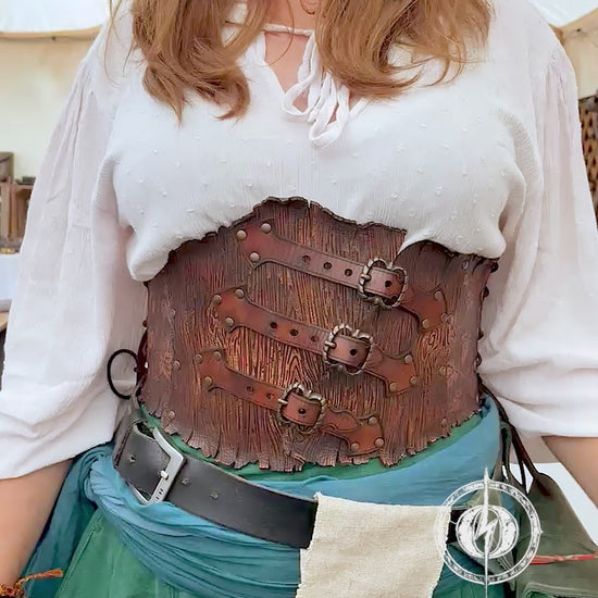 Person in a fantasy costume with 'Outcast Props' logo in the corner. Person wearing a detailed leather corset with decorative elements, branded 'Outcast Props'. Underbust Wood Leather Corset. Herbalist corset. Druid corset. Elven Corset. Ivy Corset.