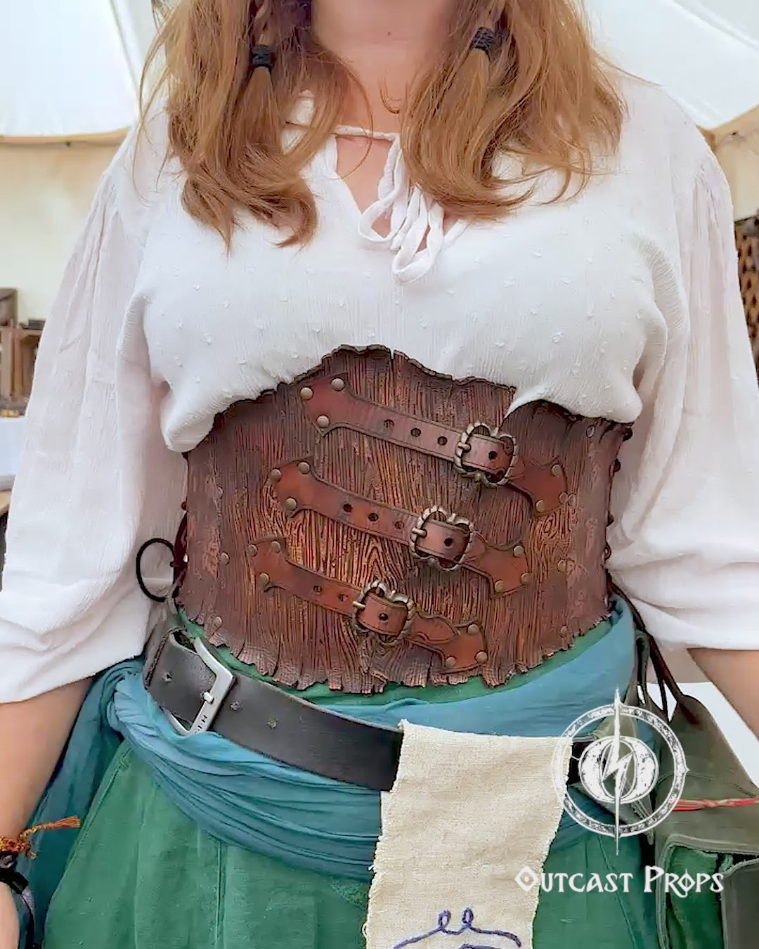 Person in a fantasy costume with 'Outcast Props' logo in the corner. Person wearing a detailed leather corset with decorative elements, branded 'Outcast Props'. Underbust Wood Leather Corset. Herbalist corset. Druid corset. Elven Corset. Ivy Corset.