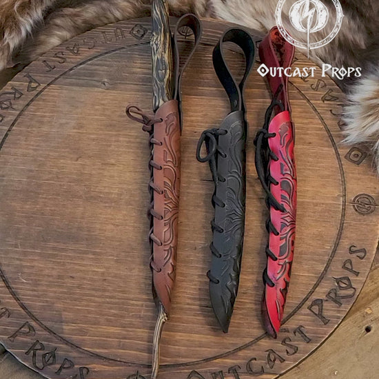 A close-up of an ornate laced leather wand holster displayed on a table with a decorative backdrop, featuring a leather-bound notebook and a candle. Magic Wand leather Holster Ornated Laced & Aged, for wizard and witch costume belt holster LARP and magic conventions and fair events
