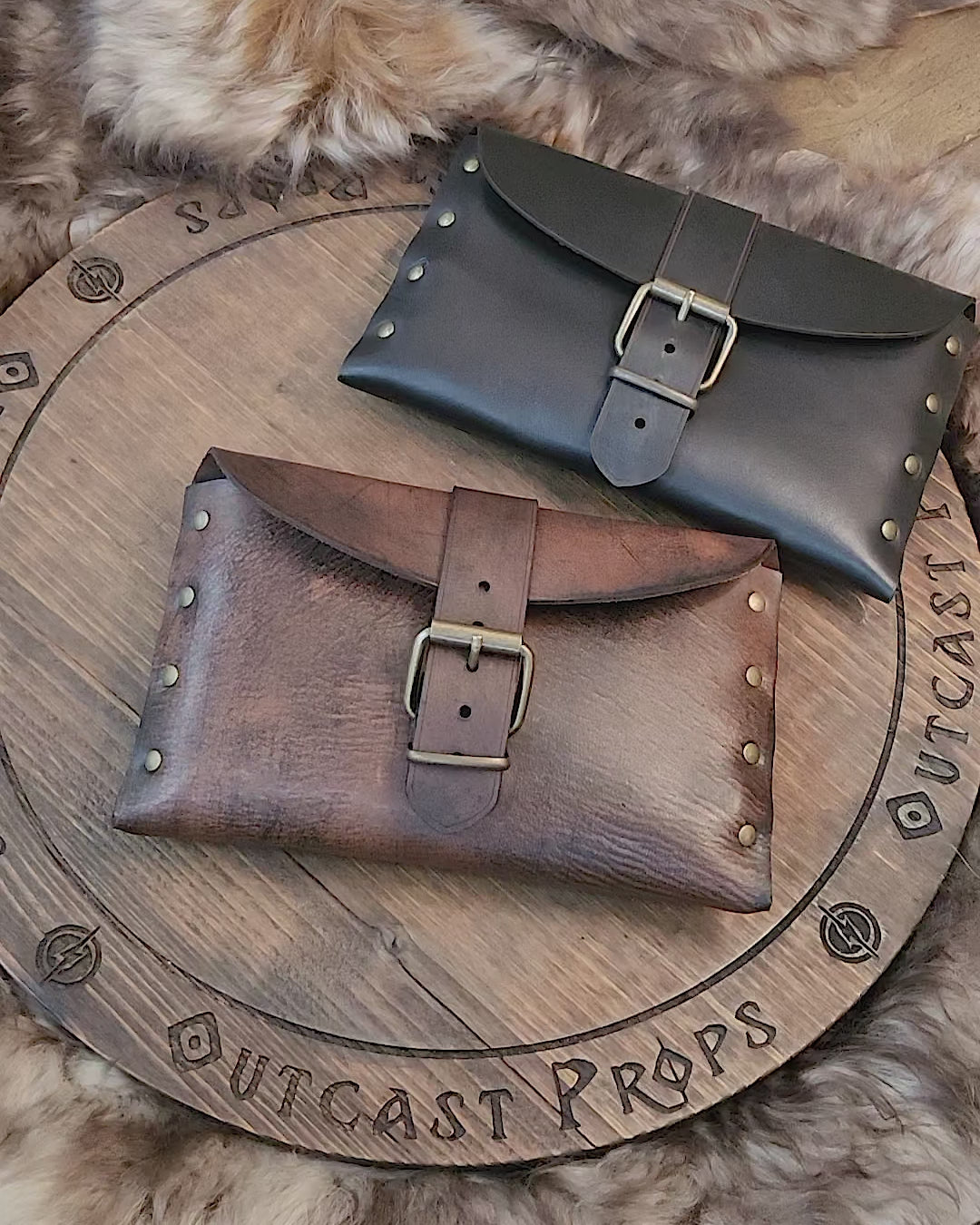 Medieval leather pouch with buckle closure placed on rustic wooden surface. Handmade Renaissance fair leather bag with natural brown tone, brass studs and curved flap. Perfect for LARP costume accessory or fantasy belt bag. Shows artisan texture of vegetable-tanned leather. Ideal for viewers needing a detailed tactile and visual description.