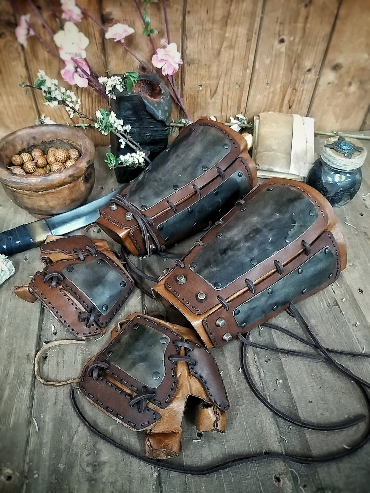 A pair of samurai armoured bracers with leather and iron components, displayed on a wooden surface with a backdrop of autumn leaves. Samurai armor iron bracers, Samurai cosplay armoured leather pair of bracers for larp, leather and Iron bracers for post apocalyptic costume