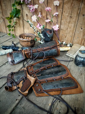 A pair of samurai armoured bracers with leather and iron components, displayed on a wooden surface with a backdrop of autumn leaves. Samurai armor iron bracers, Samurai cosplay armoured leather pair of bracers for larp, leather and Iron bracers for post apocalyptic costume