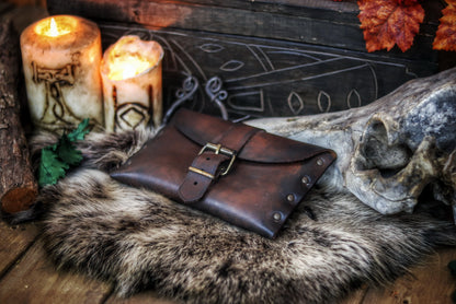 Medium brown fantasy leather belt pouch with antique brass buckle on circular wooden board engraved with Outcast Props branding. Surrounded by faux fur. Ideal for medieval scribes or LARP characters. Handcrafted pouch shows natural grain and is compatible with belts. Descriptive alt text with focus on material, use and historical style.