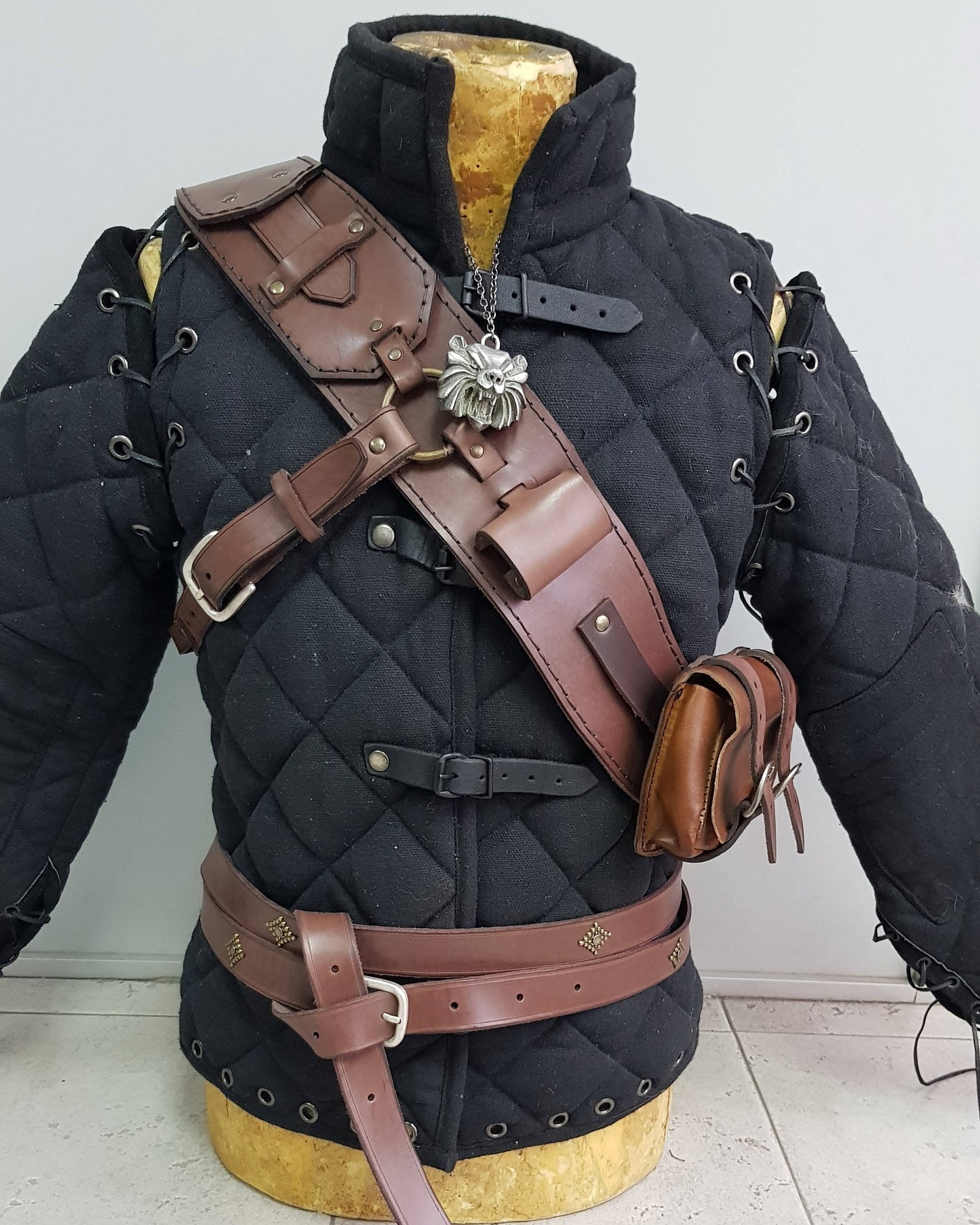 Witcher ursine baldric worn over gambeson, shown in close front view. Detailed leather work, functional pouches, iconic ring system. Ideal Witcher 3 armor cosplay, leather baldric, Geralt costume, LARP monster hunter gear, and medieval fantasy outfits.